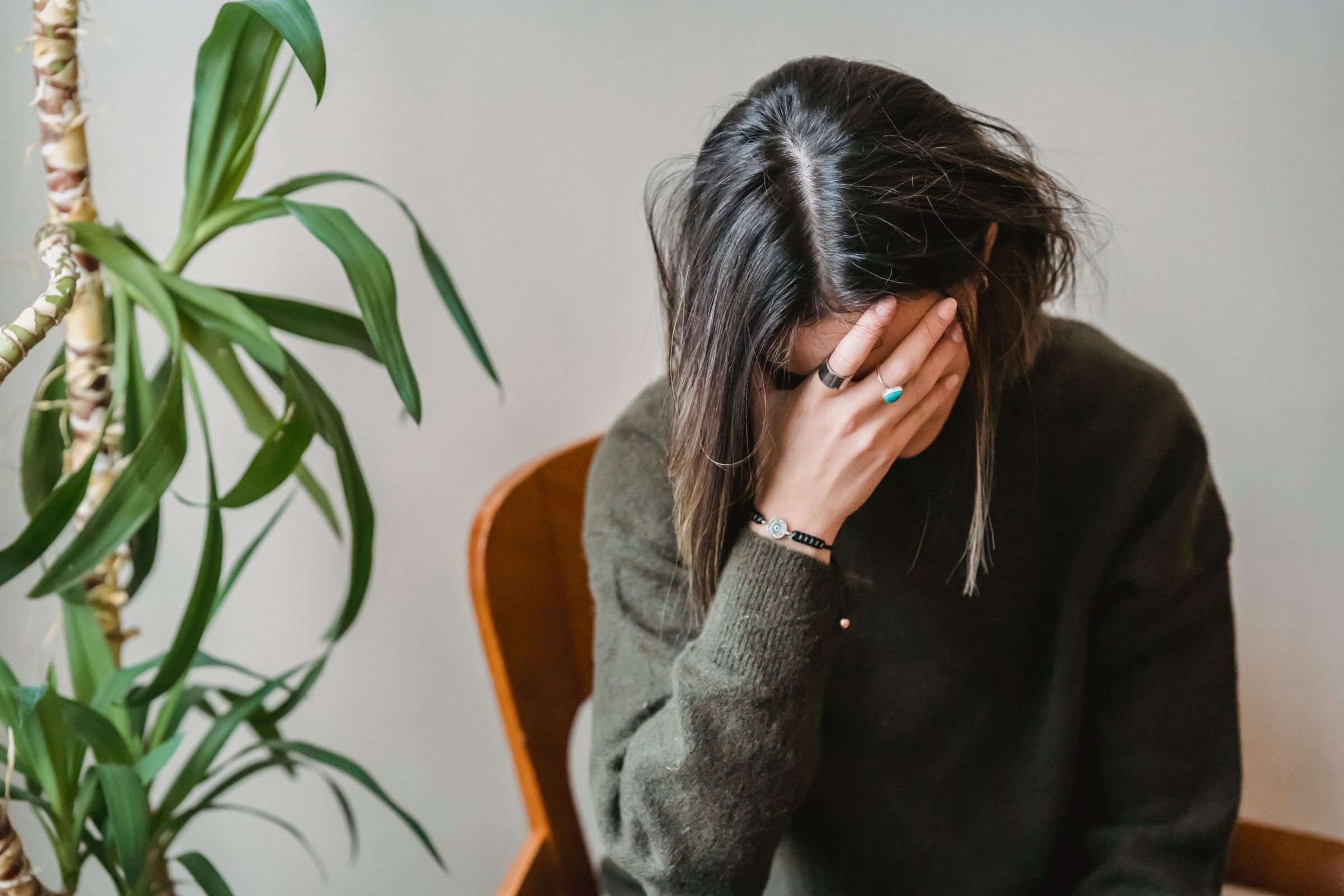 A person sitting with their head bowed and a hand covering their face